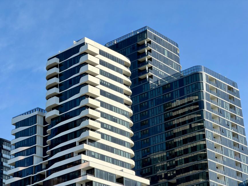 A landscape view showing the contrast between historic stone buildings with battlements and crenellations in the foreground and a cluster of modern, glass skyscrapers with reflective surfaces in the b